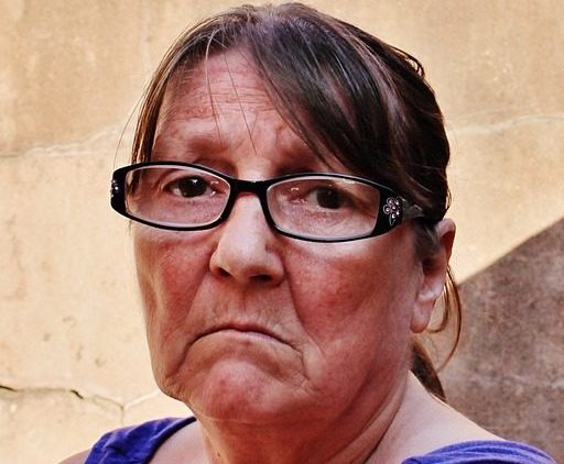 Smutná žena středního věku v brýlích s fialovým letním tričkem.
