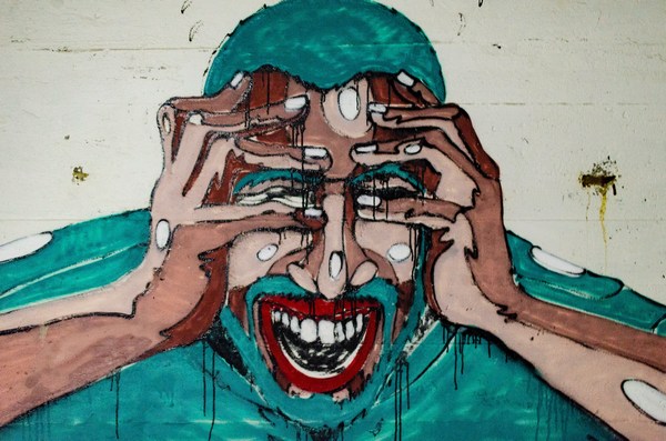 Na obrázku je nástěnná malba - graffiti - muže, který se drží za hlavu a buď se směje nebo pláče