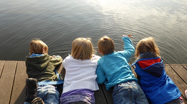 Čtyři děti leží na molu a pouštějí listy po vodě