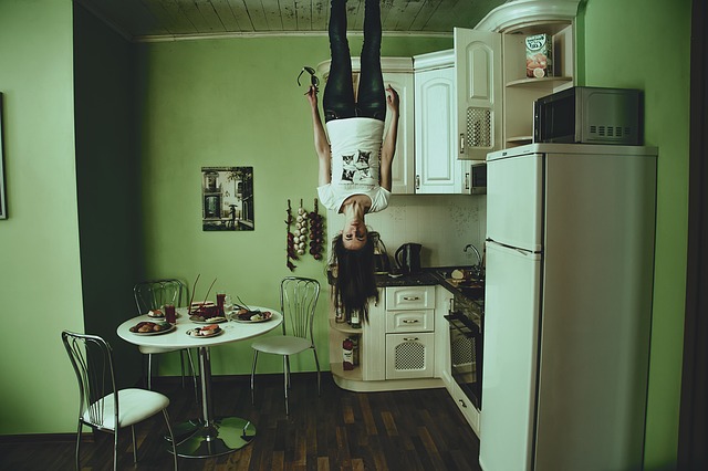 Na obrázku je žena v kuchyni, vedle lednice. Žena stojí na stropě a visí hlavou dolů.