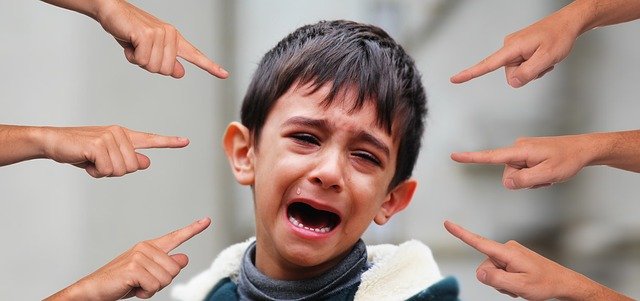 Plačící chlapec, obklopený rukama, které na něj ukazují.