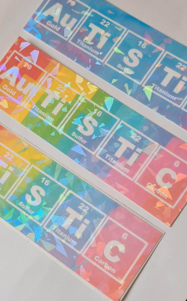 Na obrázku je na duhovém podkladu seznam prvků z periodické tabulky prvků, které dávají dohromady slovo Au Ti S Ti C. Tedy zlato, titan, síra, titan a uhlík.